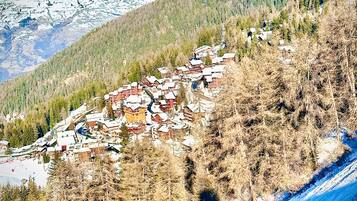 Un pueblo montañoso con casas tradicionales, una pista de esquí y un cielo despejado.