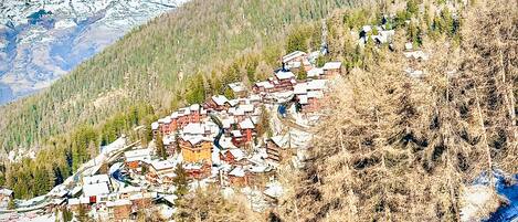 A mountainous village with traditional houses, a ski slope, and a clear sky.