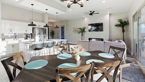 Una cocina moderna con armarios blancos, una isla central y un comedor con mesa y sillas de madera.