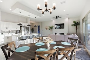 A modern kitchen with white cabinets, a central island, and a dining area with a wooden table and chairs.