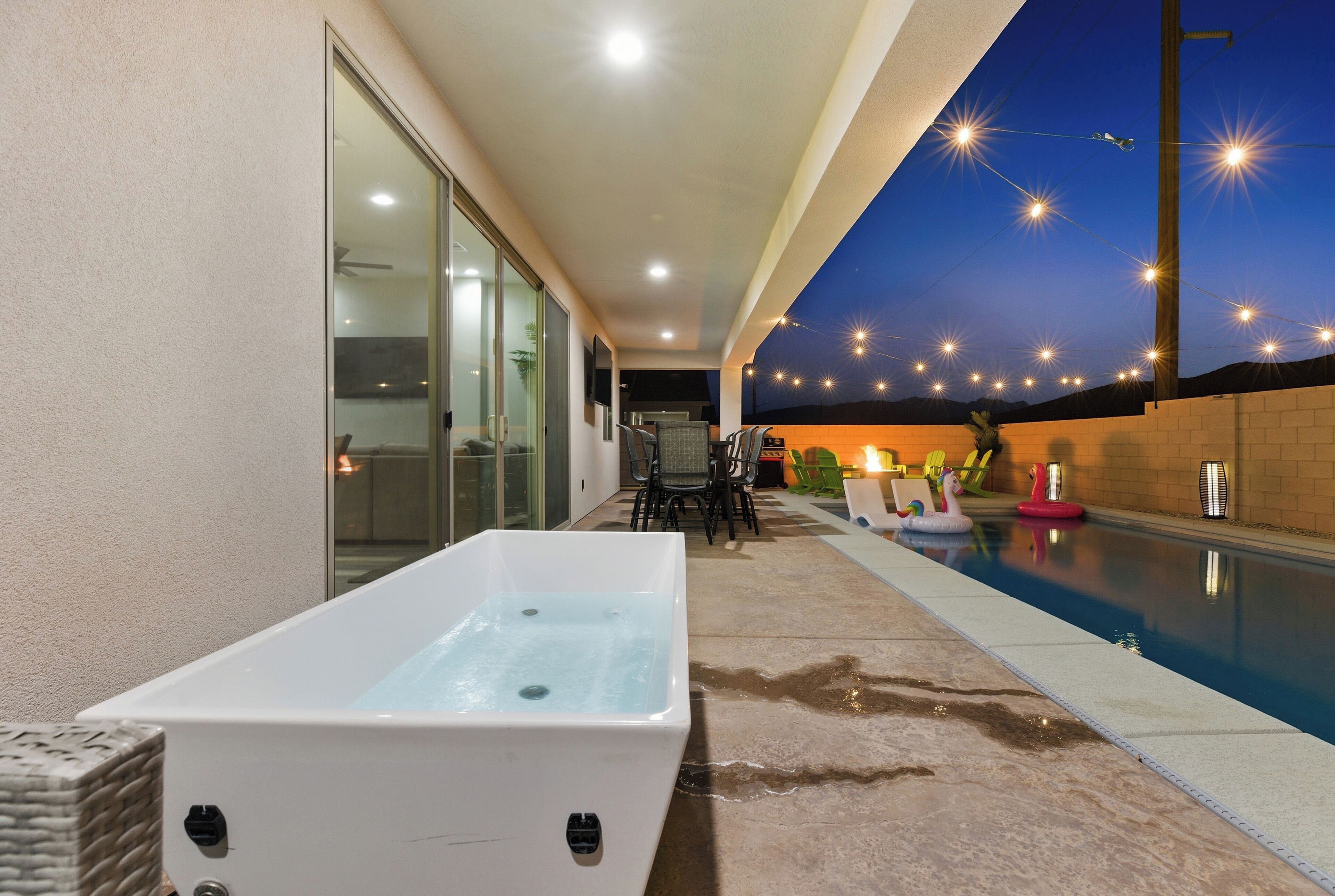 A spa area with a hot tub, outdoor seating, and a swimming pool at dusk.