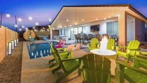 Un área de piscina moderna al aire libre con sillas verdes y una chimenea.