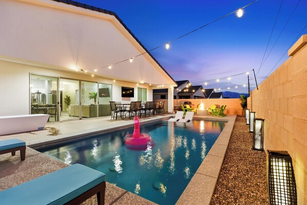 A modern outdoor pool area with a clear pool, lounge chairs, and string lights.