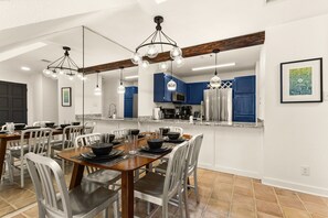 Une cuisine moderne avec des meubles bleus, un réfrigérateur en acier inoxydable et un coin repas comprenant une table en bois et des chaises blanches.
