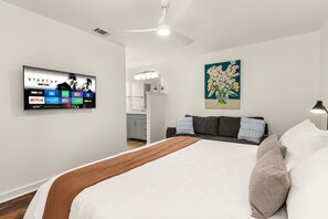 Une chambre d’hôtel avec un lit, un téléviseur fixé au mur diffusant des services de streaming, un tableau au mur et un ventilateur de plafond.