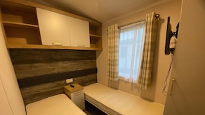Une pièce de taille modeste comprenant un lit, une petite table de chevet, une armoire et une fenêtre avec des rideaux.
