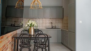 A modern kitchen with grey cabinets, a brick accent wall, a dining table with chairs, and two pendant lights. - Maszynownia by BrowarHevelius Apartments (Gdańsk)