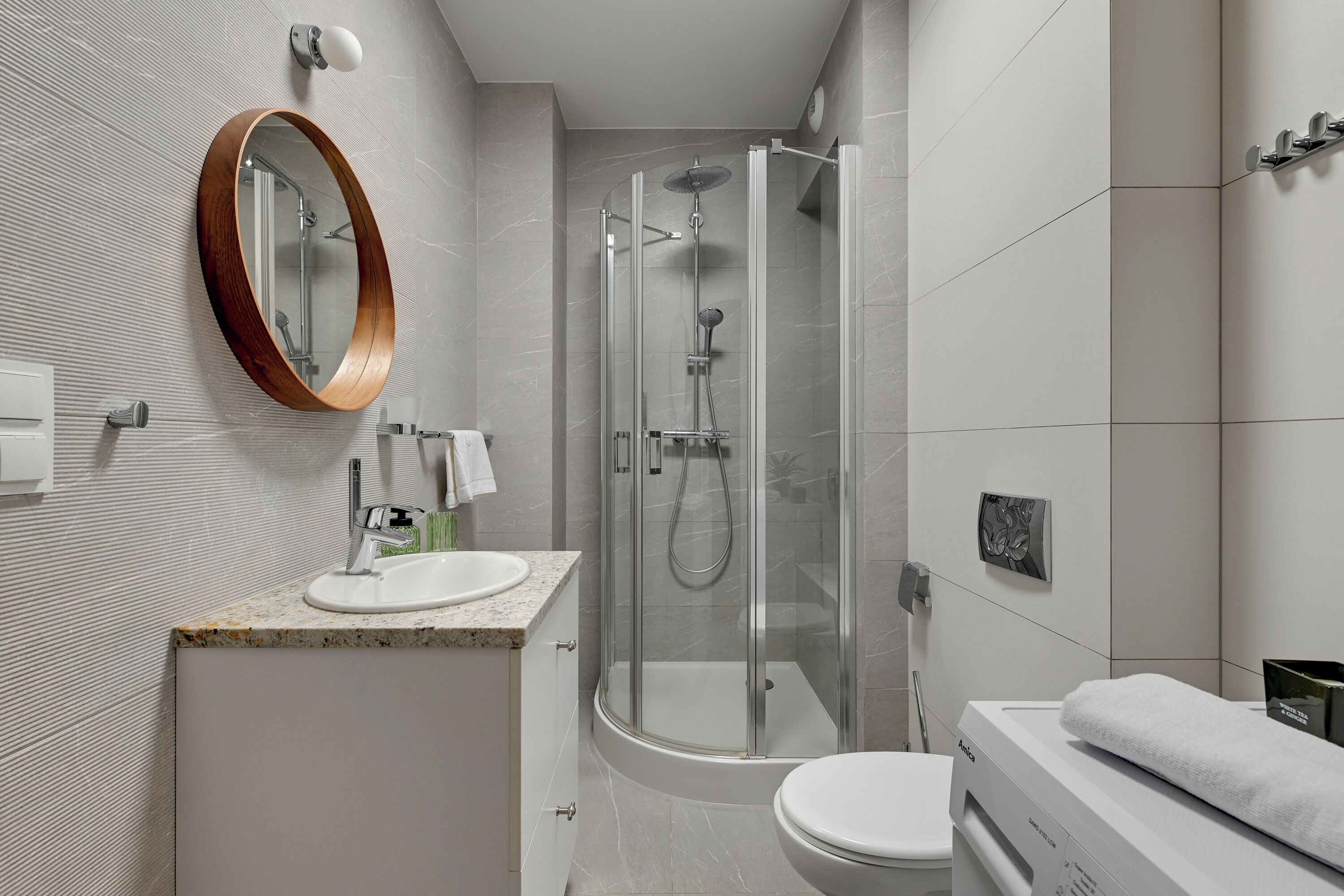 A modern bathroom with a glass-enclosed shower, a white sink with a wooden vanity, and a toilet.