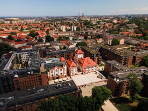 Luchtbeeld van een stadsgezicht met een opvallend gebouw met een rode dakbedekking, omringd door andere gebouwen en groen.
