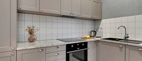 A modern kitchen with grey cabinets, a built-in oven, a sink, and a granite countertop.