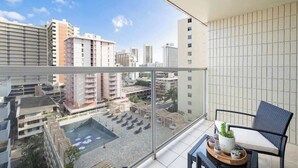 A balcony with a view of a cityscape, a seating area with a chair and a small table, and a tiled wall. - @ Marbella Lane Chic Seaside Studio w/ Pool View (Honolulu)