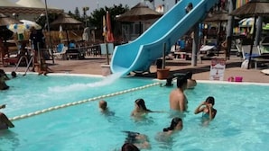 Zona de piscina con un tobogán azul, sillas de descanso y sombrillas.