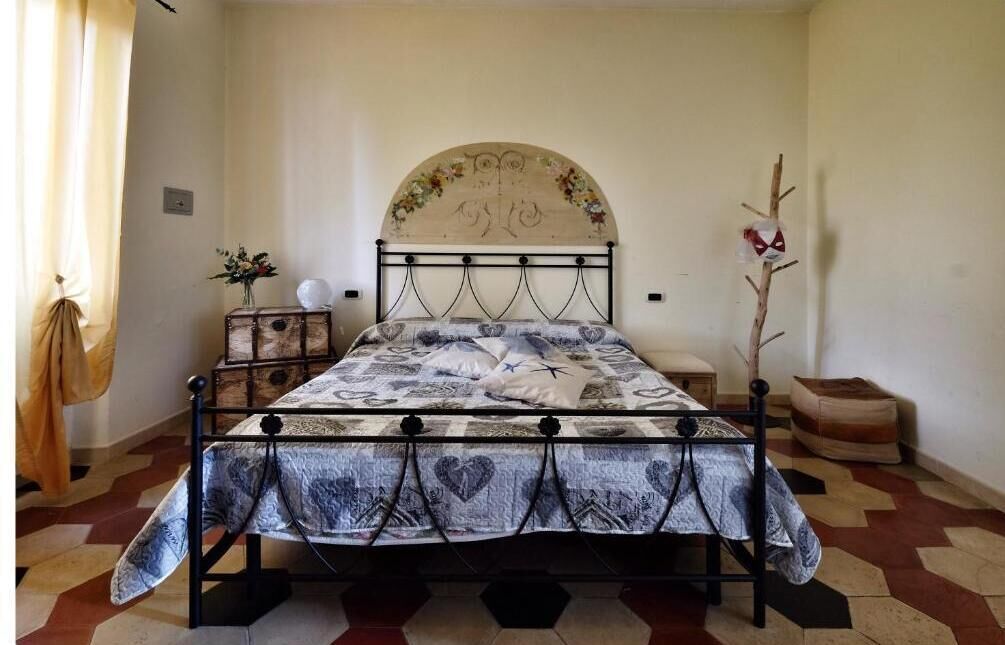 A bed with a floral headboard, a bedside table with a vase, and a geometric patterned floor.