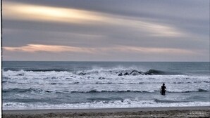 Una playa con olas y una persona caminando en el agua.
