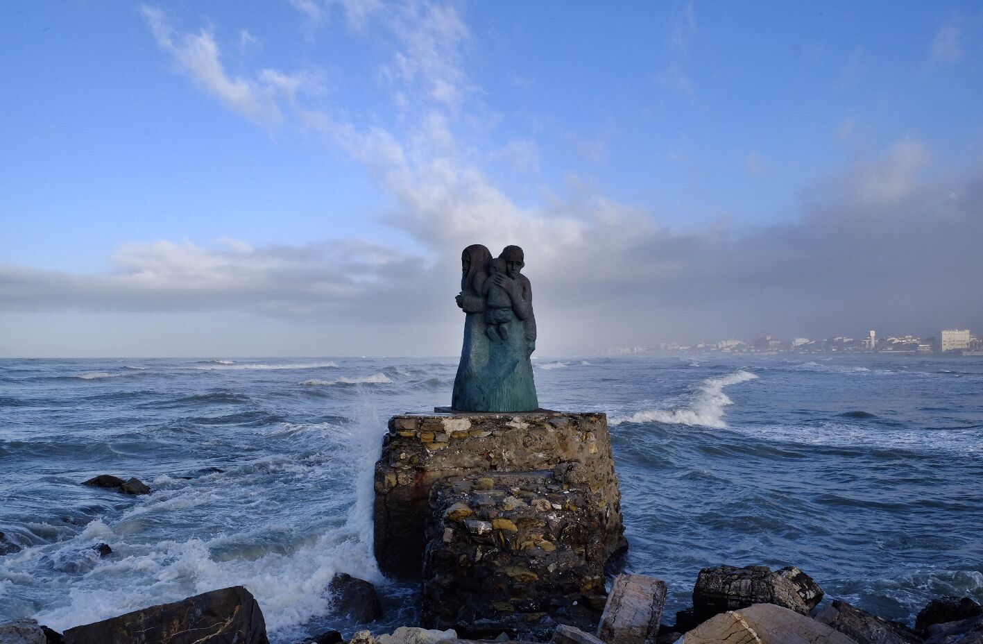 A statue of two figures embracing on a rocky outcrop by the sea.