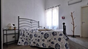 Un dormitorio con cama, mesita de noche, lámpara, ventana con cortinas y puerta.
