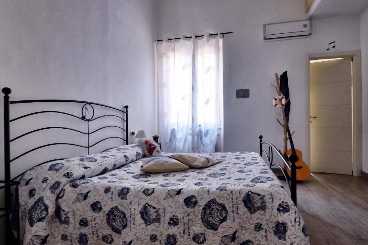 A bedroom with a bed, a guitar, and a door leading to another room.