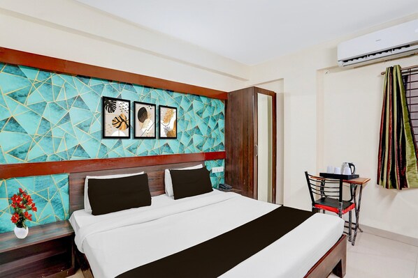 A hotel room with a bed, a small table with a chair, a wall-mounted air conditioner, and a door. - Classic Hotel Shree Krishna Avenu (Indore)