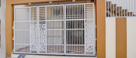 Une entrée fermée par un portail en métal, un escalier et la façade d’un immeuble.