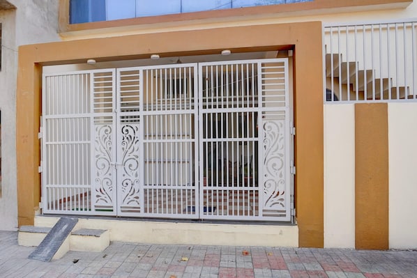 Une entrée fermée par un portail en métal, un escalier et la façade d’un immeuble.