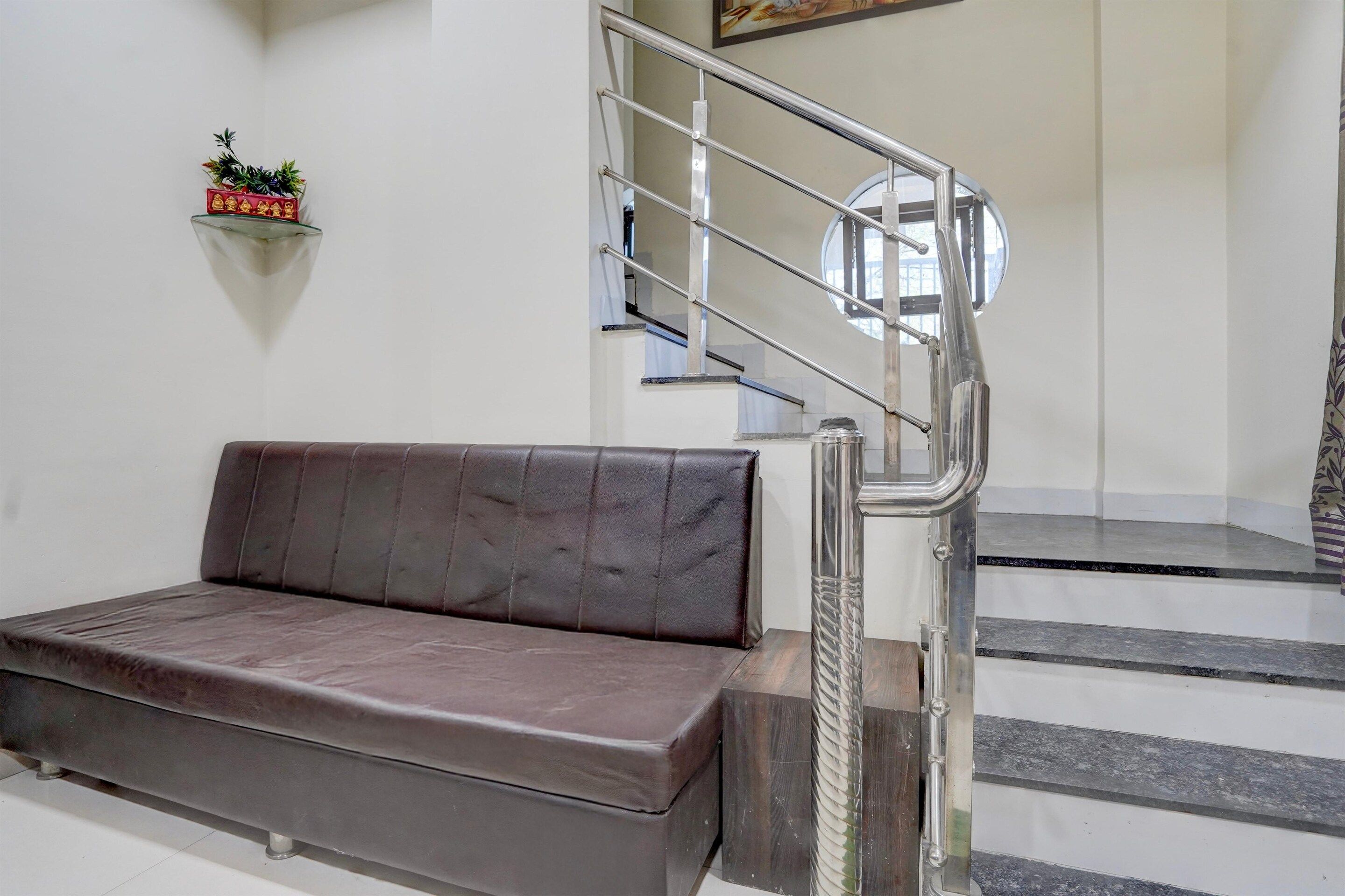 A modern interior with a sofa, a staircase with a metal railing, and a wall-mounted shelf with a plant.