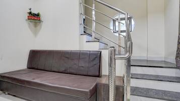 A modern interior with a sofa, a staircase with a metal railing, and a wall-mounted shelf with a plant.