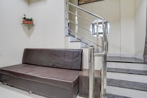 A modern interior with a sofa, a staircase with a metal railing, and a wall-mounted shelf with a plant.