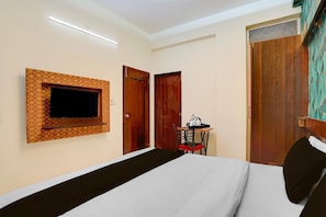 Une chambre d’hôtel comprenant un lit, un téléviseur fixé au mur, un bureau avec une chaise et deux portes en bois.
