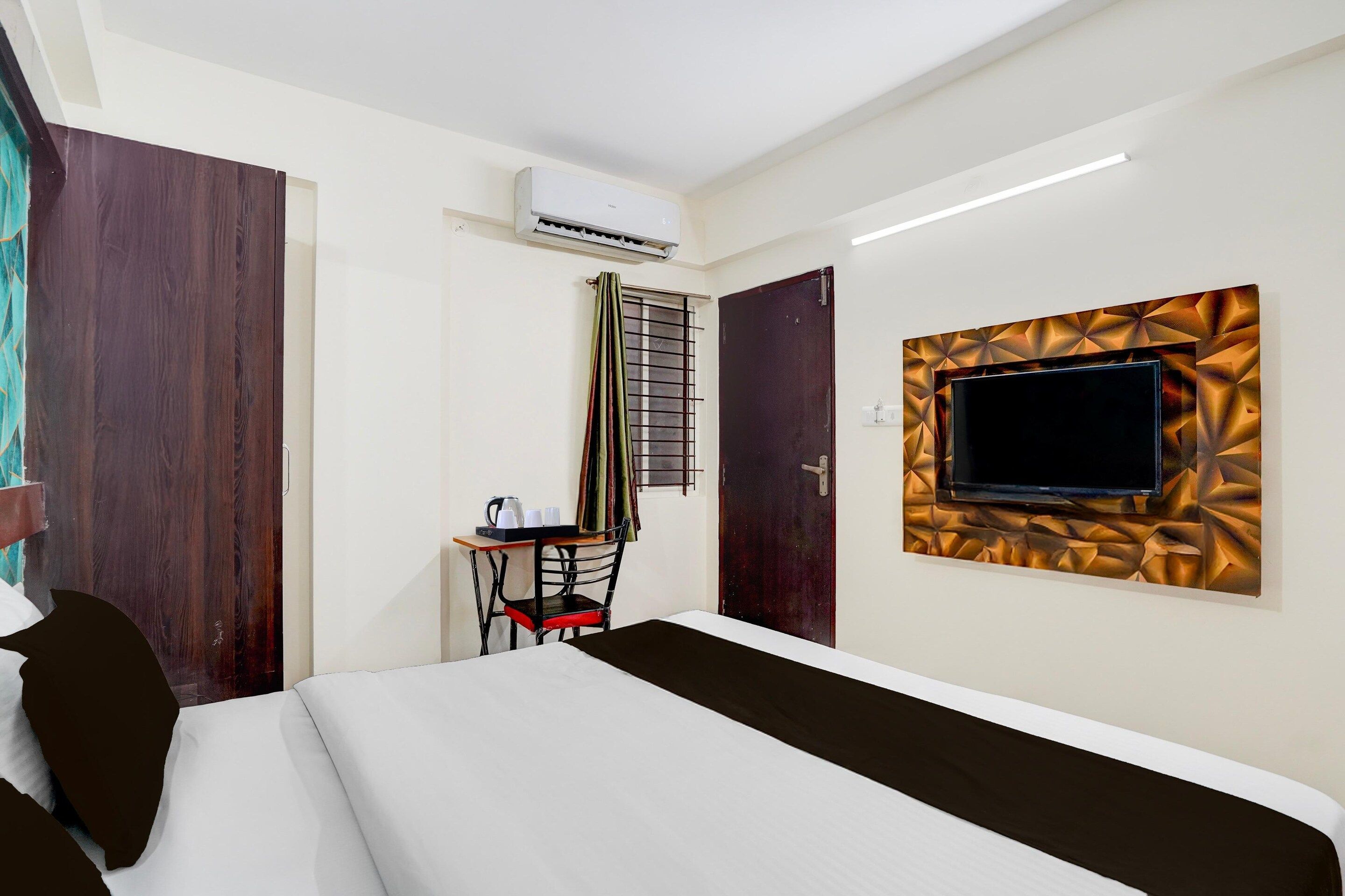 Une chambre d’hôtel comprenant un lit, un bureau avec une chaise, un appareil de climatisation, un téléviseur fixé à un mur texturé et une porte.