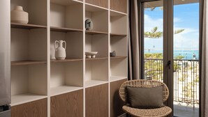 Ein Zimmer mit einer Holzhockerreih, einem Korbstuhl und Blick auf das Meer durch eine Glastür.