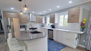 A modern kitchen with a central island, white cabinetry, and stainless steel appliances. - INDOOR POOL, HOT TUB & SAUNA!!  Welcome to Bluehaven in the Kawartha's!! (Buckhorn)