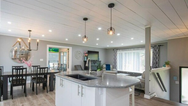 A modern kitchen with a central island, pendant lighting, and a dining area with chairs. - INDOOR POOL, HOT TUB & SAUNA!!  Welcome to Bluehaven in the Kawartha's!! (Buckhorn)