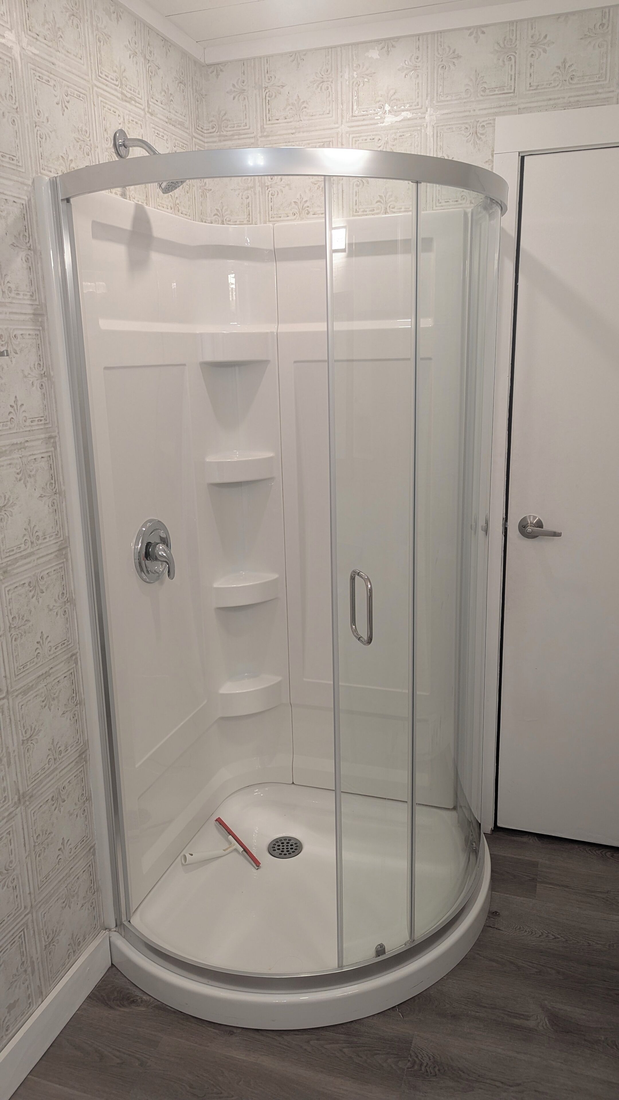 A glass-enclosed shower with a white door and a metal handle.