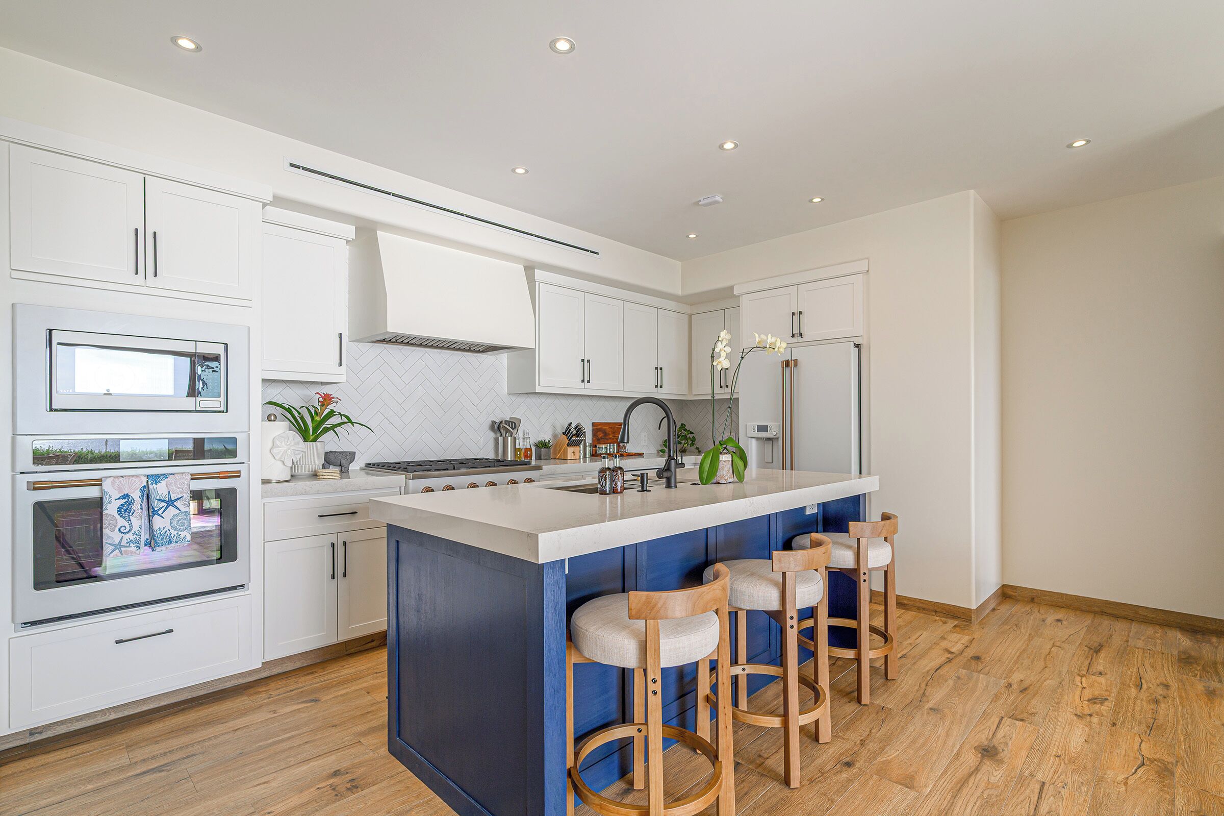 A modern kitchen with white cabinets, a blue island, and wooden bar stools.