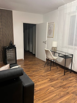 Ein Hotelzimmer mit Holzboden, einem schwarzen Ledersofa, einem kleinen Schreibtisch mit Stuhl, einer Lampe und einem gerahmten Bild an der Wand.