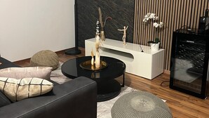 A modern living room with a black sofa, a round coffee table, a white console table, a television mounted on the wall, and a black speaker. - Dream house in Düsseldorf (Düsseldorf)