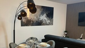 A dining area with a round table set for six, surrounded by six chairs. A modern floor lamp with three shades is positioned above the table. A large abstract painting hangs on the wall above the table. - Dream house in Düsseldorf (Düsseldorf)