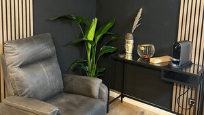 A corner room with a black wall, a leather chair, a small table with a plant, a decorative vase, and a coffee machine. - Dream house in Düsseldorf (Düsseldorf)