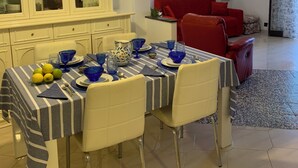 Ein Essbereich mit einem für vier Personen gedeckten Tisch, einer Schranke mit Glastüren, einem roten Sofa und einem Fernseher im Hintergrund.