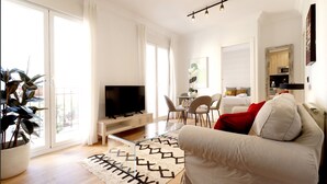 Un salon moderne avec un téléviseur à écran plat, un canapé, un coin repas avec des chaises et une cuisine en arrière-plan.