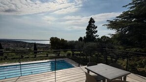 A poolside area with a table and chairs, a view of the sea, and a clear sky. - Agriturismo Collina del Lago (Lazise)