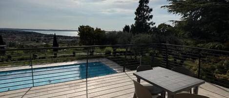 A poolside area with a table and chairs, a view of the sea, and a clear sky.