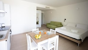 A compact hotel room with a kitchenette, a dining area with a table and chairs, a bed, and a green sofa. - Agriturismo Collina del Lago (Lazise)