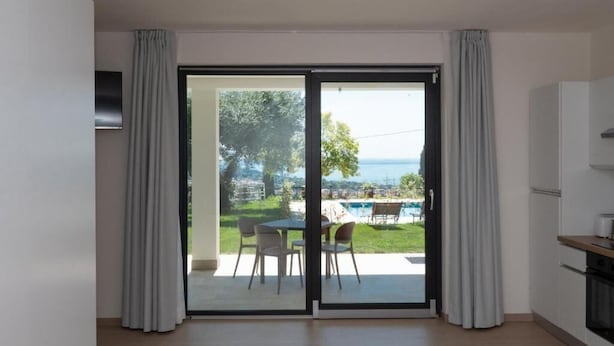 A modern apartment with a sliding glass door leading to a balcony with a pool and outdoor furniture. - Agriturismo Collina del Lago (Lazise)