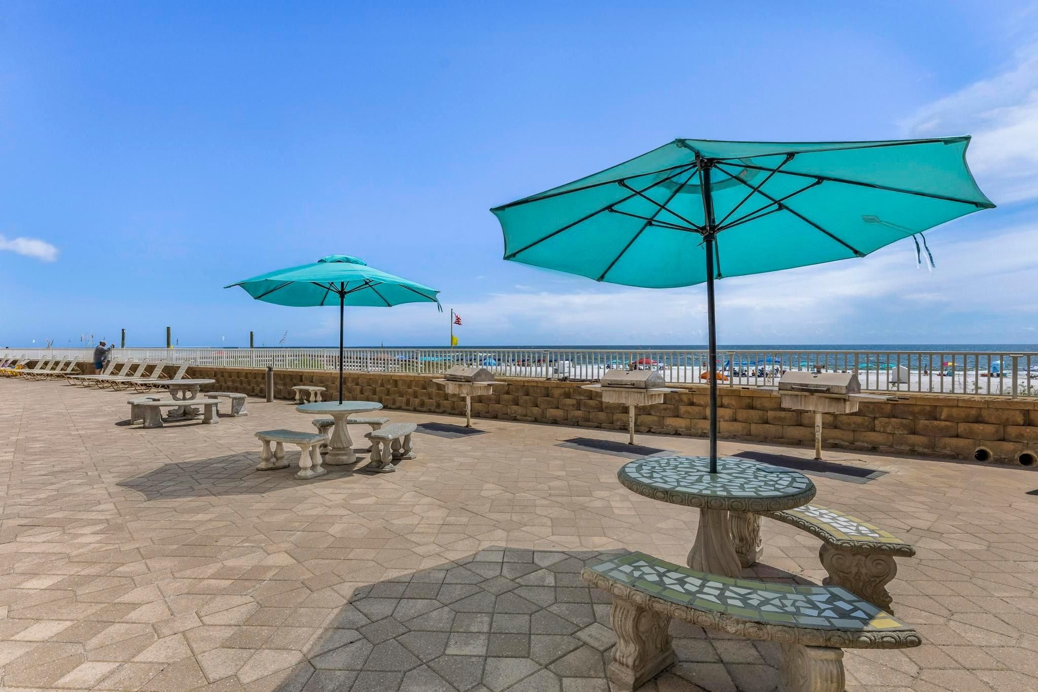 An outdoor seating area with tables and chairs, a stone wall, and a view of the beach.