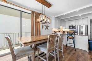 A modern kitchen with white cabinets, a wooden dining table, and a hanging light fixture. - Romar Place 506 (Orange Beach)