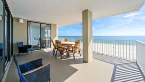 Een balkon met een tafel en stoelen, uitzicht op de oceaan en een glazen deur die naar een kamer leidt.