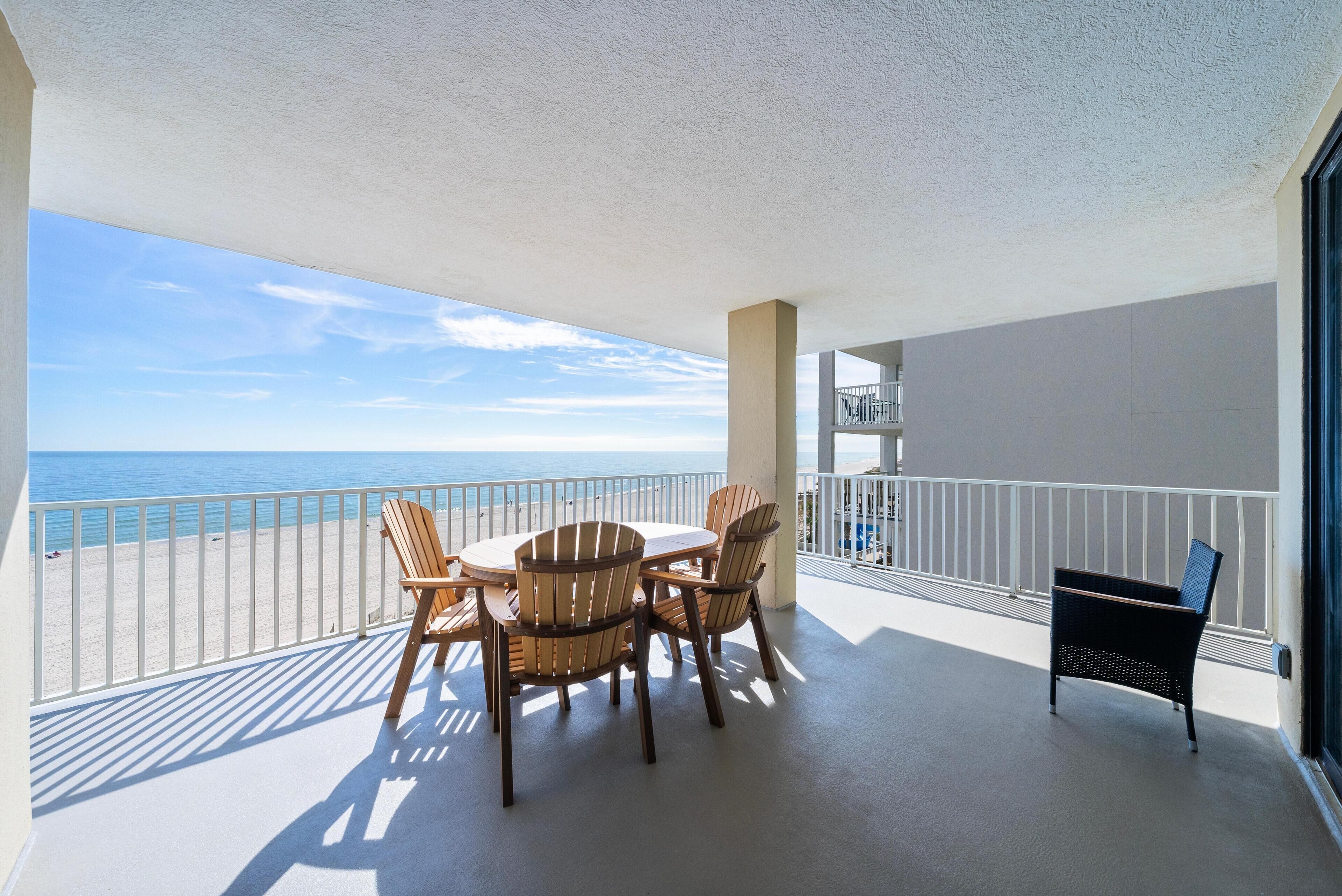 A balcony with a table and chairs, overlooking a beach.