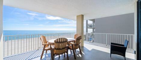 A balcony with a table and chairs, overlooking a beach.