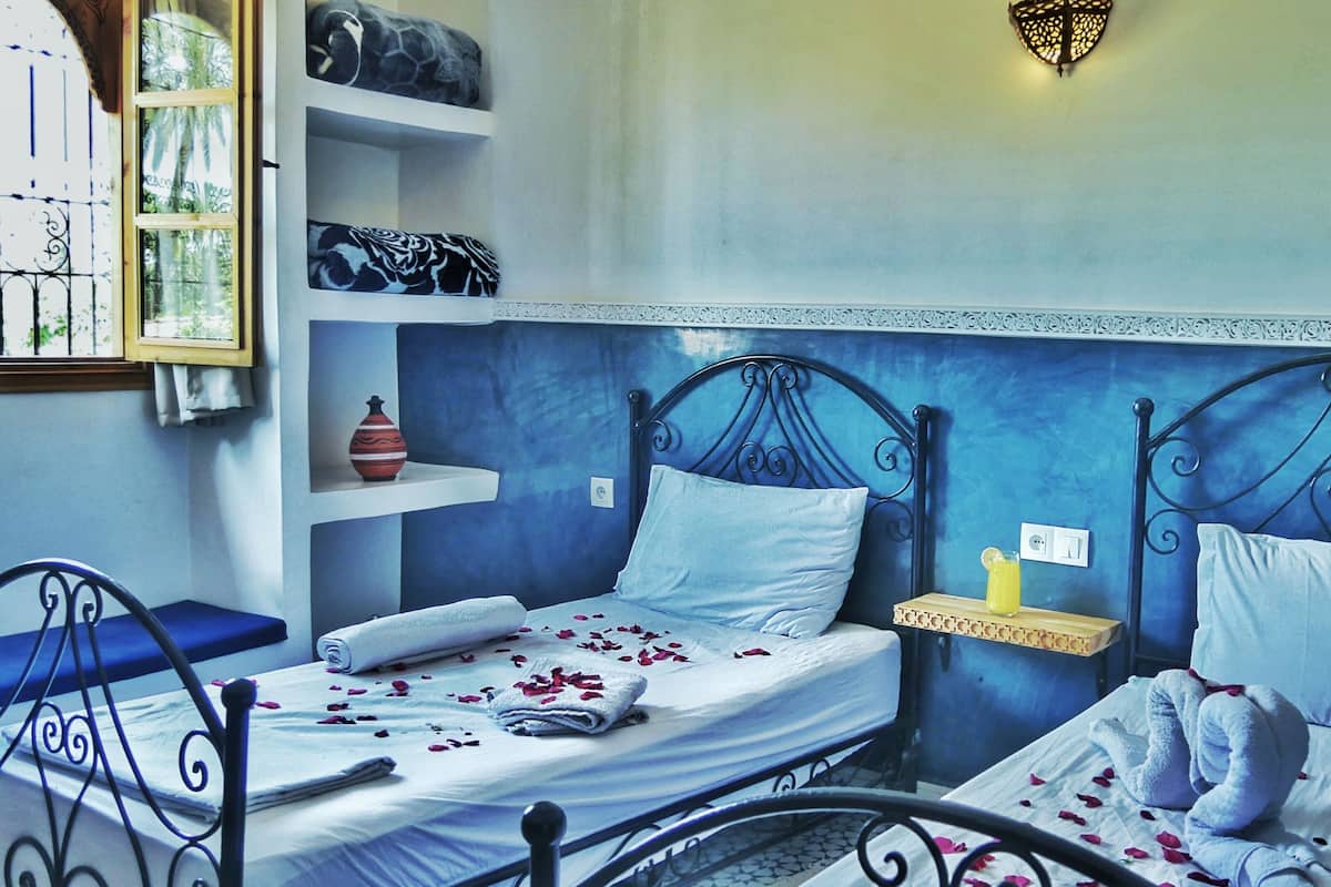 A bedroom with two beds, a bedside table, a chair, and a decorative wall.